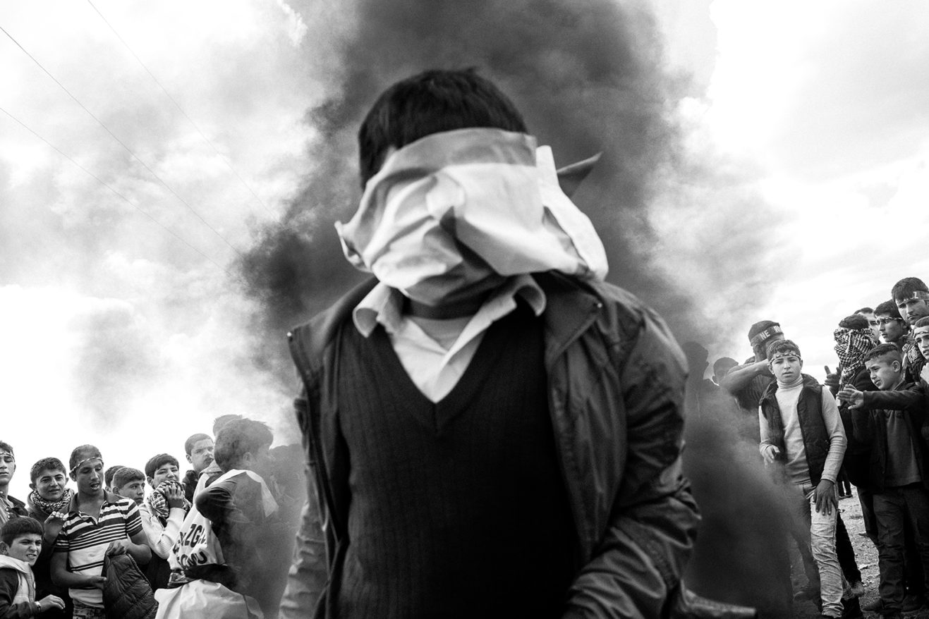 During Newroz, people build large fires and jump over them. In this photo, a child jumps over the fire with a YPG (the Kurdish People’s Protection Units) flag tied over his face. March 17, 2016. Suruç, Şanlıurfa, Turkey.