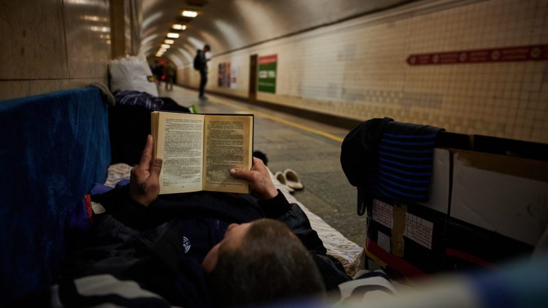 A person reclines on an underground subway platform, reading.