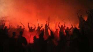Silhouette of a crowd of people wielding swords against a fiery background, as if to suggest war.