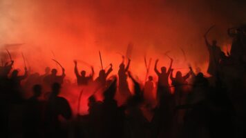 Silhouette of a crowd of people wielding swords against a fiery background, as if to suggest war.