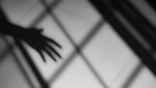 Black and white image of shadows of a window pane and a hand reaching outward.